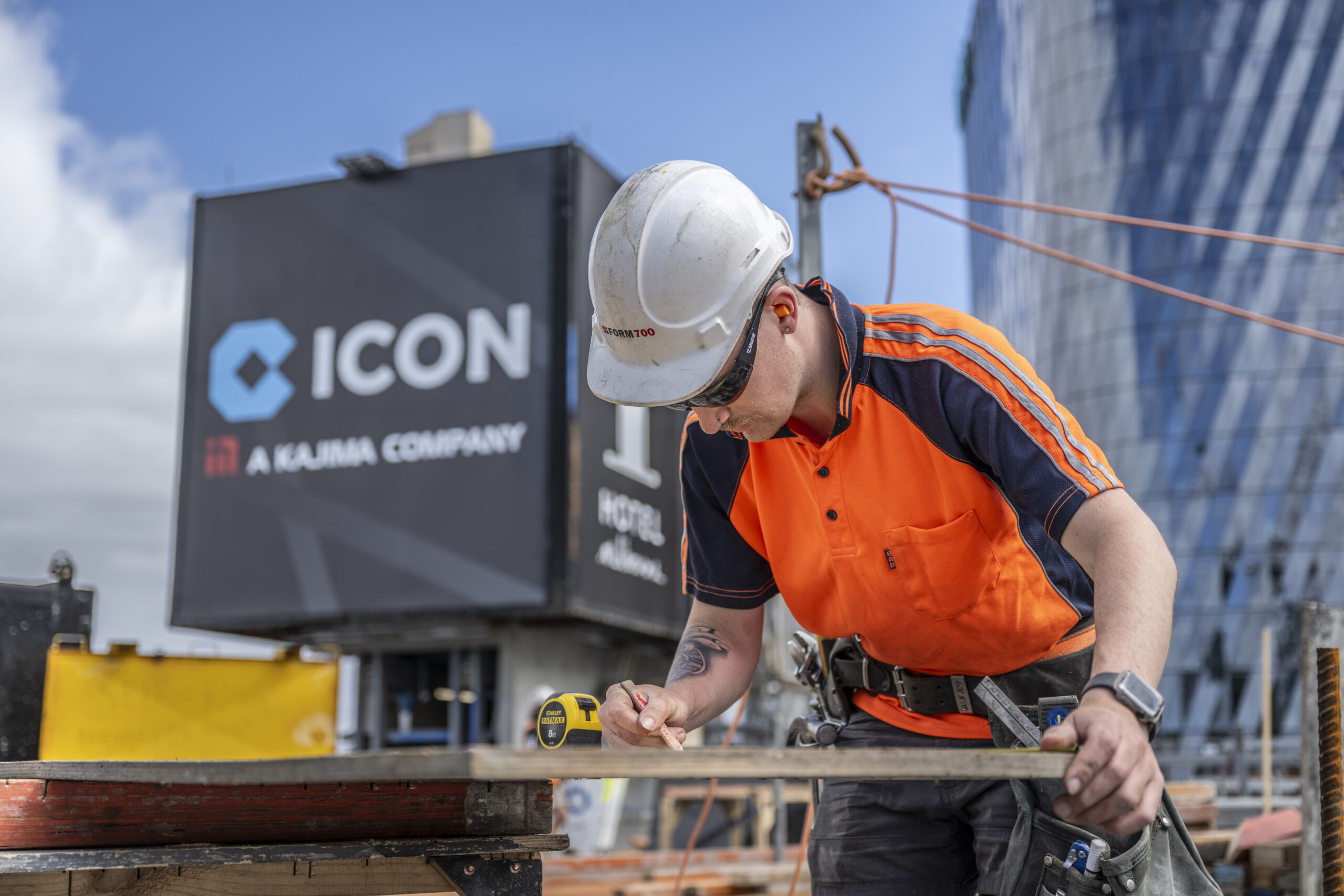 An Icon site team member measuring timber in front of an Icon-branded hoarding