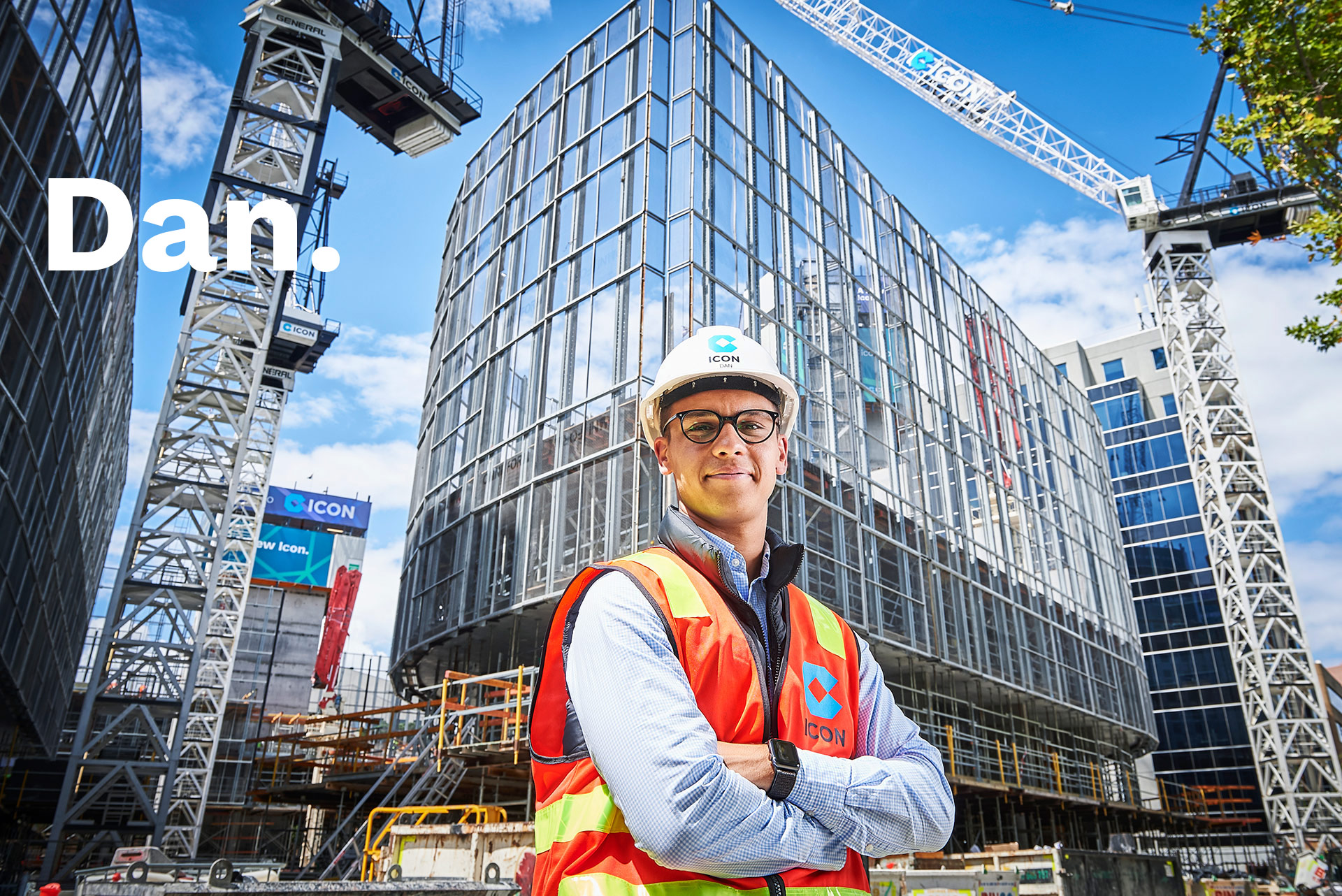 An Icon site manager standing in front of a glass tower under construction, cranes overhead